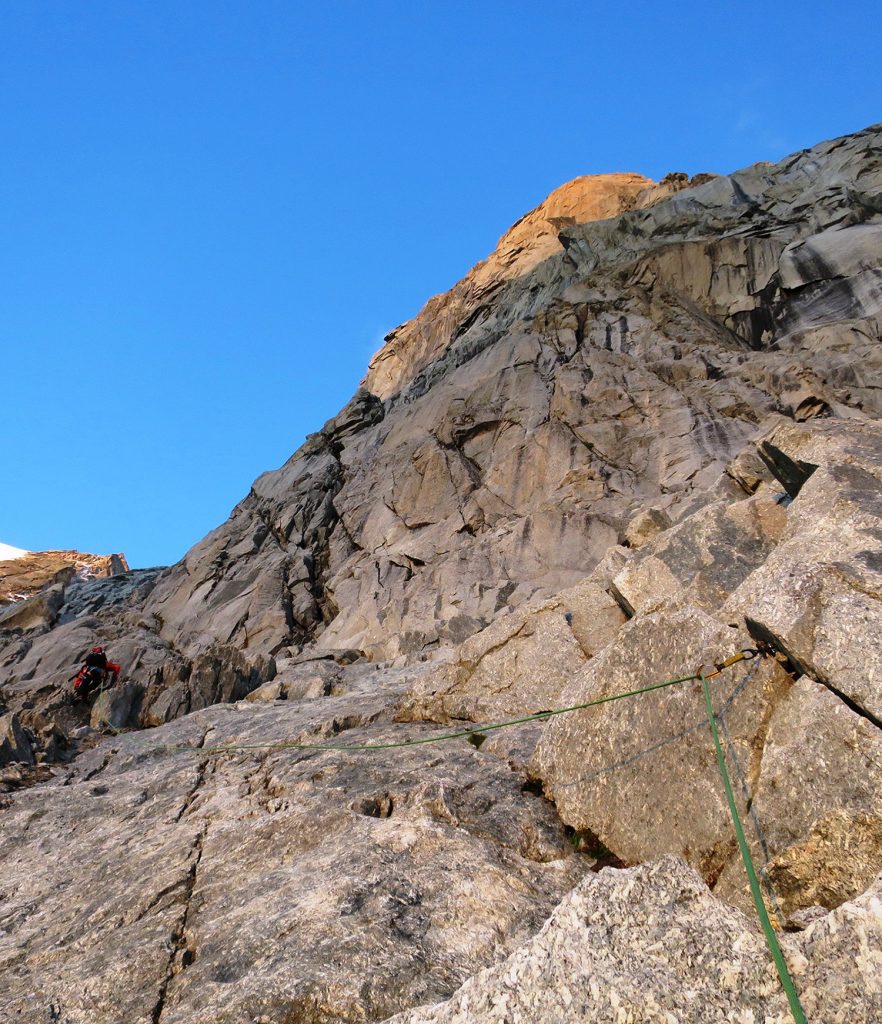 Maroš v spodnej časti piliera, súbežné lezenie. Východom slnka ožiarený monolit vysoko nad nami
