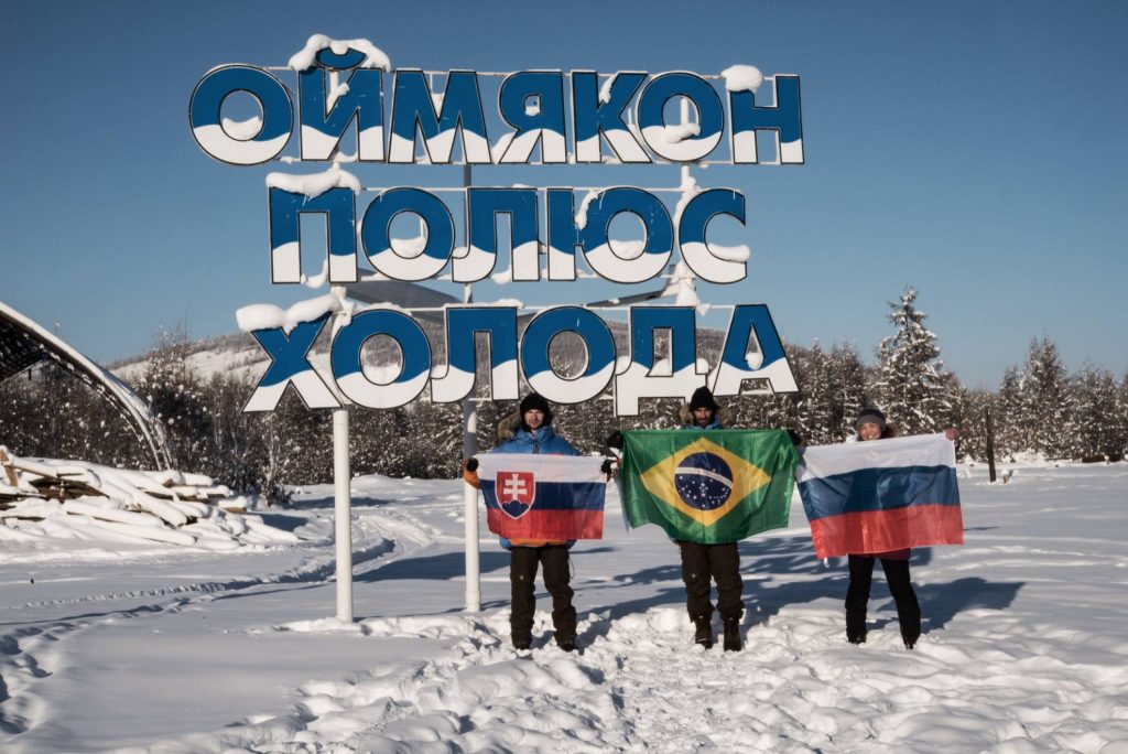 Dominik a jeho kolegovia s vlajkami pred nápisom "Oymyakon, Pól chladu"